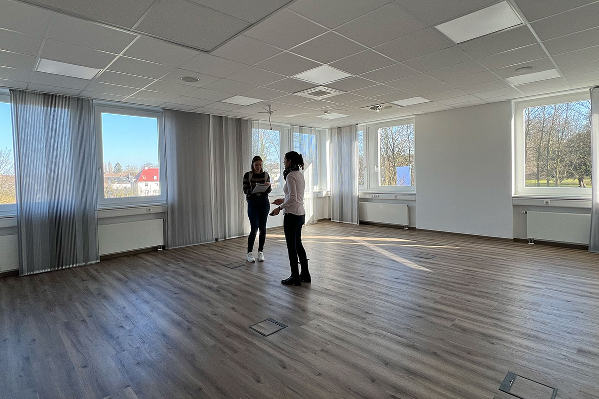 Zwei Personen stehen in einem leeren großen Raum und planen die Gestaltung